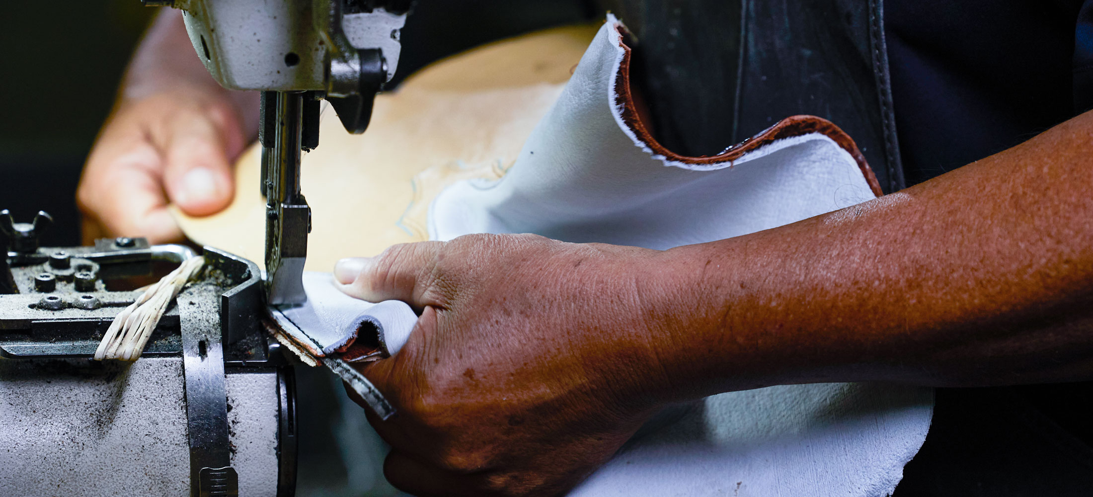 Hands sewing leather boots together.